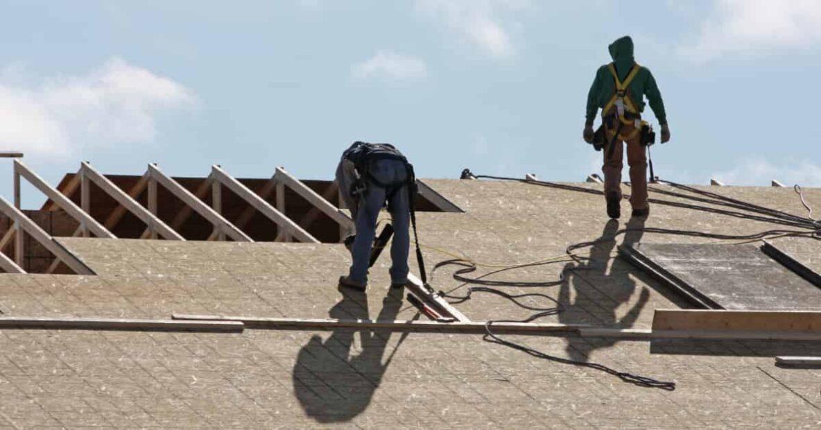 Two construction workers are seen on a roof, likely working on its installation or repair.